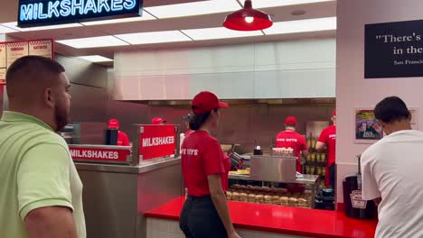 Five-Guys-fast-food-burger-restaurant,-people-waiting-for-their-order,-employees-working-in-the-kitchen,-4K-shot