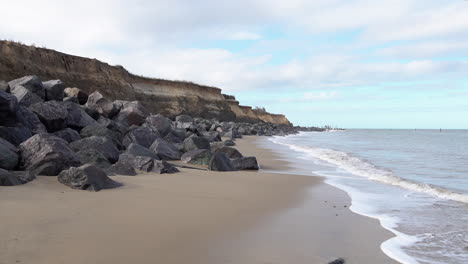 Wellen-Rollen-Von-Der-Nordsee-Auf-Einen-Strand,-Der-Durch-Einen-Meeresschutz-Aus-Granitfelsen-An-Der-Durch-Küstenerosion-Beschädigten-Küste-Von-Norfolk-Geschützt-Ist