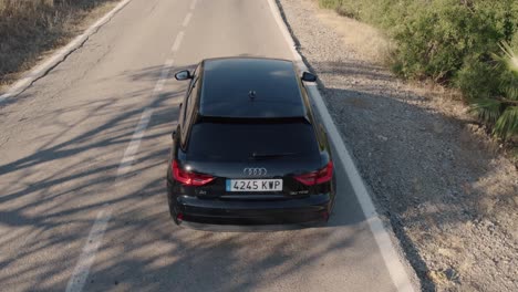 Following-drone-shot-over-a-black-mercedes-sedan-along-rural-countryside-in-El-Torcal-de-Antequera,-Sierra-in-Spain-at-daytime