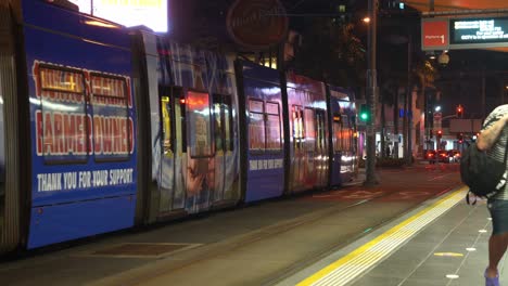 Tranvía-Saliendo-De-La-Plataforma-En-La-Avenida-Cavill-Por-La-Noche,-Paraíso-De-Los-Surfistas,-Barrio-Del-Centro,-Costa-Dorada,-Queensland,-Australia