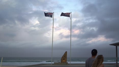 Statische-Aufnahme-Am-Anzac-denkmal-Mit-Australien--Und-Neuseeland-flaggen,-Die-Kräftig-Durch-Den-Starken-Und-Wütenden-Wind-Wehen,-Mit-Dramatischen-Dunklen-Ominösen-Wolken,-Die-über-Den-Himmel-An-Der-Goldküste,-Queensland,-Fegen