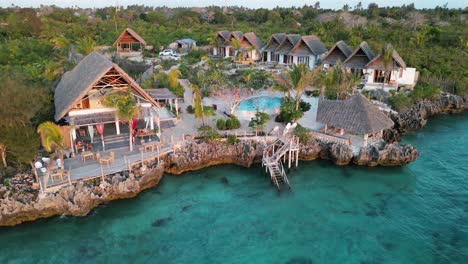 Turistas-En-El-Complejo-De-Bungalows-De-Playa-En-La-Piscina-Cerca-Del-Océano-índico,-Toma-De-Pedestal-Aéreo-En-Ascenso