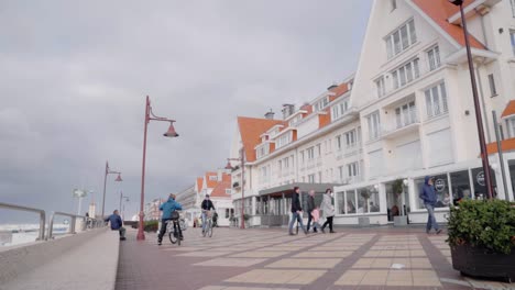 Gente-En-El-Paseo-Marítimo-De-La-Playa-De-Haan-Con-Tiendas-Frente-Al-Mar-Durante-El-Día-En-De-Haan,-Bélgica