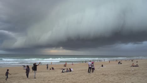 Toma-Panorámica-A-La-Izquierda-A-Través-De-La-Playa-Costera-En-El-Paraíso-De-Los-Surfistas,-Una-Gruesa-Capa-De-Ominosas-Nubes-Oscuras-De-Tormenta-Que-Se-Extienden-Por-El-Cielo,-Gente-Viendo-Un-Clima-Apocalíptico-En-Gold-Coast,-Queensland