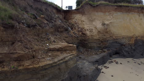 Eine-Luftaufnahme-Erhebt-Sich-Vom-Strand,-Um-Zu-Zeigen,-Wo-Die-Küstenerosion-Eine-Straße-Zerstört-Hat-Und-Nahe-Gelegene-Häuser-An-Der-Küste-Von-Norfolk-Bedroht