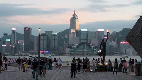 A-crowd-of-local-people-and-tourists-are-seen-at-the-Victoria-Harbour-waterfront-as-they-enjoy-their-evening,-sunset,-and-skyline-view-of-Hong-Kong-Island-skyscrapers