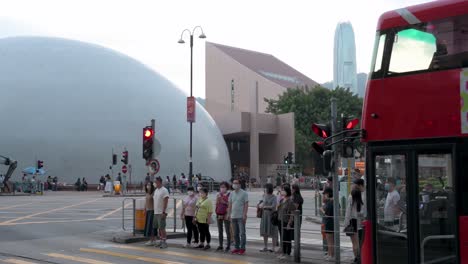 Pedestrians-and-commuters-wait-at-a-traffic-light-as-they-are-about-to-walk-through-a-zebra-crossing-with-the-Space-Museum,-known-for-its-hemispherical-shape,-seen-behind-them-in-the-background