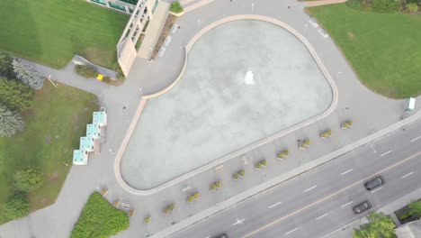 Sich-Langsam-Nach-Unten-Bewegende-Aufnahmen-Von-Oben-Eines-Teichs-Mit-Springbrunnen-Vor-Einem-Großen-Gebäude-Mit-Blauem-Dach