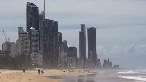 Gente-Paseando-Por-La-Playa-De-Arena-Dorada-Con-Propiedades-De-Inversión-De-Gran-Altura-En-El-Fondo,-Popular-Destino-Turístico-En-Verano-En-Broadbeach-Gold-Coast,-Queensland,-Australia