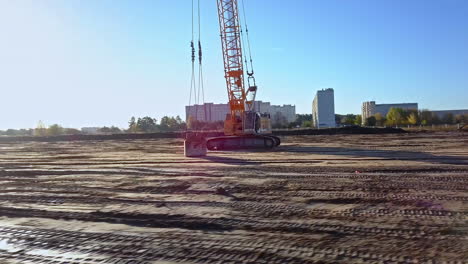 Aerial-drone-rotation-over-static-yellow-crane-in-sandy-construction-site