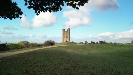 Dramatische-Luftaufnahme-Des-Broadway-Tower,-Cotswolds,-Großbritannien,-Enthüllung-Vom-Baum,-Aufsteigender-Schuss-über-Türmchen-Und-Union-Jack-Flagge