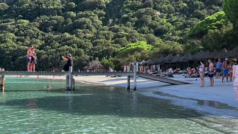 Frau-Macht-Foto-Von-Stehendem-Paar-Auf-Holzsteg-Mit-Telefon-Am-Strand-Von-Santa-Giulia-Auf-Der-Insel-Korsika,-Frankreich