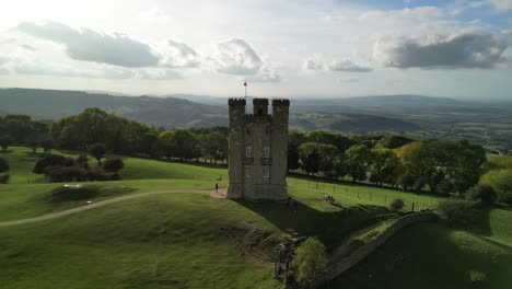 Dramatic-wide-aerial-helix-shot-of-Broadway-tower,-an-English-landmark-stood-atop-Beacon-Hill-in-the-Cotswolds,-UK