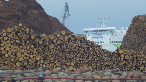 Big-ferry-ship-Stena-Line-parked-at-Port-of-Liepaja-,-overcast-autumn-day,-distant-medium-shot-trough-piles-of-wood