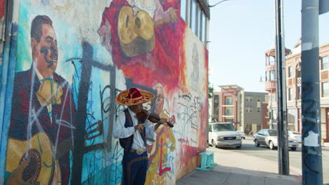 Mariachi-Square-Los-Angeles,-a-mariachi-musician-plays-on-the-violin-against-a-mural