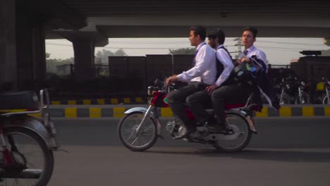 Tráfico-De-Cerca-Toma-Panorámica-En-La-Carretera-Bajo-El-Sobrevuelo,-Pasando-Motos-Y-Coches,-Bicicletas,-Autobuses,-Rickshaw,-Vallas-Publicitarias-Y-Edificios-En-El-Fondo