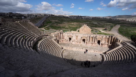 Panoramablick-Auf-Das-Nördliche-Theater-Von-Jerash-In-Römischen-Ruinen-Mit-Touristen,-Die-Auf-Der-Steintreppe-Spazieren-Gehen,-Und-Wolken,-Die-Schatten-Auf-Den-Theaterplatz-Werfen