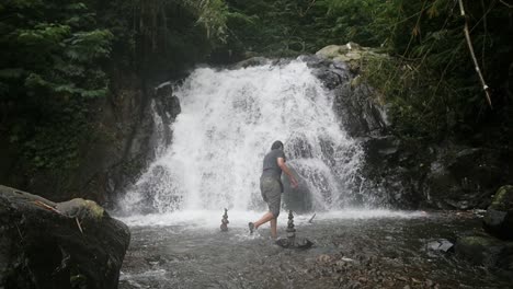 Indonesian-man-building-cairns-in-a-river-in-front-of-a-waterfall