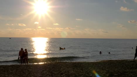 Tourists-walking-on-the-beach-at-sunset,-people-playing-frisbee