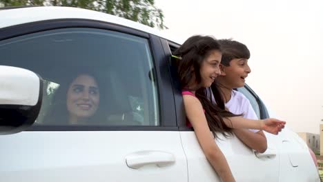 Mama-Fährt-Ein-Weißes-Auto,-Während-Ihre-Beiden-Kinder-Beim-Bewegen-Vor-Freude-Halb-Vor-Dem-Fenster-Lächeln