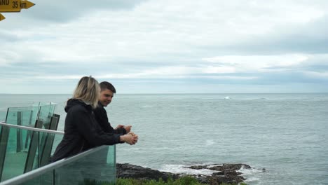 Pareja-Joven-Y-Atractiva-Mirando-El-Océano-Por-El-Signo-De-Stirling-Point-En-Bluff,-Nueva-Zelanda