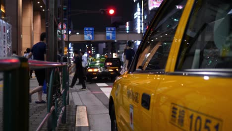 Tokio-Taxi-Bei-Nacht,-Mit-Der-Reflexion-Des-Taxischildes-Im-Seitenspiegel-Des-Taxis-Und-Passanten-Im-Hintergrund