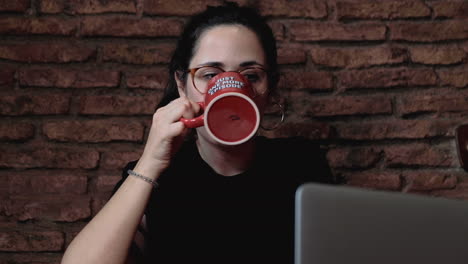 Primer-Plano-De-Una-Joven-Y-Hermosa-Morena-Con-Gafas-Mirando-La-Computadora-Y-Bebiendo-Café-De-Una-Taza-Con-La-Inscripción-&quot;solo-Un-Episodio-Más