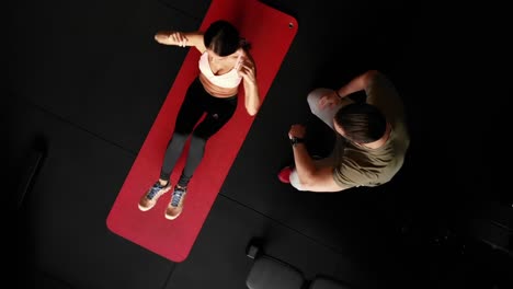 Disparo-De-Dron-Giratorio-De-Arriba-Hacia-Abajo-De-Una-Mujer-Deportiva-Haciendo-Ejercicio-En-Una-Alfombra-Con-Entrenador-Personal