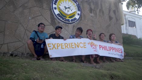 Young-people-smile-and-wave-as-they-shake-a-white-banner-with-Experience-Philippines-written-across-it