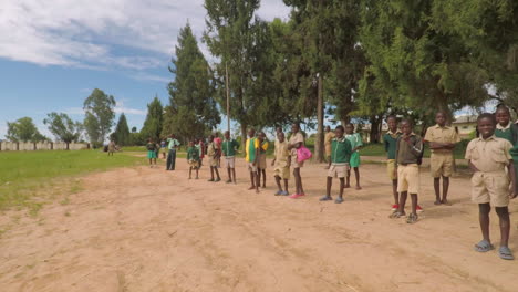 Running-by-a-Crowd-of-African-Children-Watching-a-Soccer-Game-Outside-of-their-School,-Slow-Motion