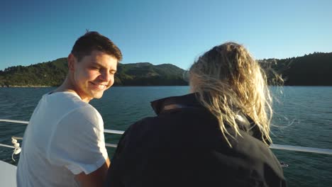 Pareja-Joven-Sentada,-Hablando-Y-Disfrutando-De-La-Noche-Durante-La-Puesta-De-Sol-En-Un-Barco-En-Los-Sonidos-De-Marlborough,-Nueva-Zelanda