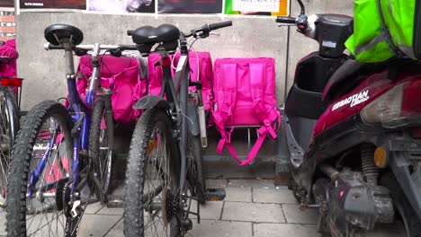 Fahrräder-Und-Taschen-Für-Die-Lieferung-Von-Lebensmitteln,-Die-In-Urbaner-Umgebung-An-Der-Wand-Aufgereiht-Sind