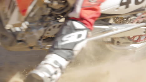 SLOW-MOTION:-A-dirt-biker-rides-his-red-motorcycle-through-the-desert-and-whips-around-a-berm