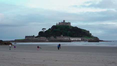 Niños-Jugando-Con-Una-Cometa-En-La-Playa-De-Marazion-En-Cornualles-Con-El-Castillo-Medieval-Inglés-Y-La-Iglesia-Del-Monte-De-San-Miguel-Detrás