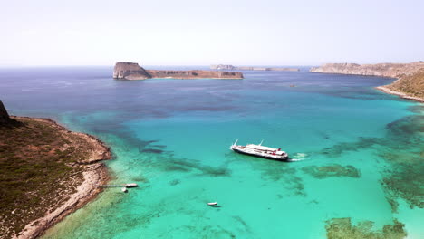 Toma-Aérea-Estática-De-Un-Crucero-De-Un-Día-Maniobrando-En-La-Playa-De-Balos-En-Creta,-Grecia-En-Hermosas-Aguas-Turquesas-En-Un-Día-Soleado