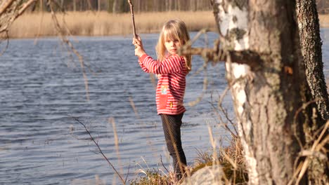 Niña-Jugando-Con-Un-Palo-Cerca-Del-Agua