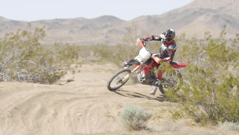 Cámara-Lenta:-Un-Motociclista-Conduce-Su-Motocicleta-Roja-Por-El-Desierto-Y-Gira-Alrededor-De-Una-Berma