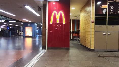 Editorial,-Vista-De-Lapso-De-Tiempo-Del-Logotipo-De-Mcdonald&#39;s-En-La-Pared-Al-Lado-Del-Vestíbulo-De-Entrada,-Entrada-Del-Restaurante-De-Comida-Rápida,-Que-Muestra-A-La-Gente-Y-Los-Clientes-Pasando-En-Movimiento-De-Lapso-De-Tiempo