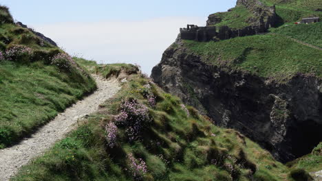 Tourist-on-vacation-walking-on-top-of-a-cliff-along-the-path-that-leads-to-the-ruins-of-Tintagel-castle-in-Cornwall