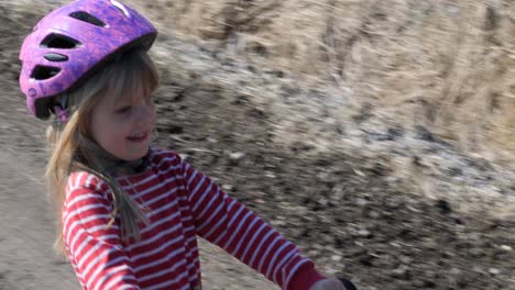 Una-Niña-Pequeña-Monta-Una-Bicicleta-En-Un-Camino-De-Grava-En-Un-Paisaje-Rural,-Una-Buena-Manera-De-Lograr-El-Equilibrio-Para-Que-Los-Niños-Aprendan