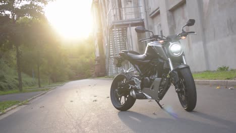 Toma-Panorámica-De-Una-Motocicleta-Con-Luz-Led-Frente-A-Un-Edificio-Industrial-Y-Puesta-De-Sol-En-El-Fondo