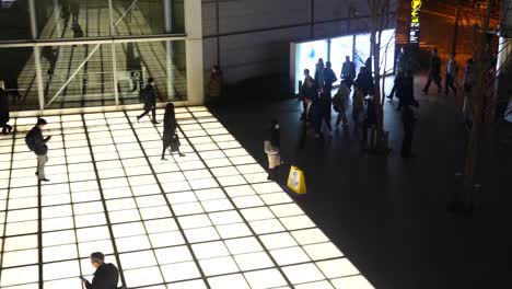 Yurakucho-Station---Tokyo-International-Forum-Bei-Nacht-Mit-Vorbeifahrenden-Pendlern,-Kameraschwenks-Von-Rechts-Nach-Links-Auf-Den-Quadratischen-Lichterboden-Vor-Dem-Forum