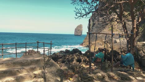 Couple-sitting-on-a-swing-set-at-the-ocean-at-Tembeling-pools-in-Bali,-Indonesia