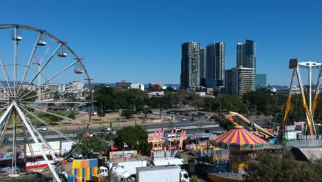 Aerial-view-of-a-beach-side-carnival-next-to-a-busy-main-road-with-buildings-in-the-background