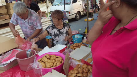 Hombre-Y-Mujer-Vendiendo-Pan-Local-En-El-Mercado-Callejero-Con-Gente-Comprando-El-Pan