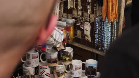 Hombre-Recogiendo-Tazas-De-Diseño-Sirio-Y-Colocándolas-En-Pirámide,-Los-Recuerdos-Cuelgan-En-El-Fondo