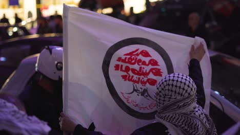 A-protester-in-Beirut-Lebanon-holds-a-flag-on-a-busy-street,-his-head-is-covered-in-a-traditional-Lebanese-scarf