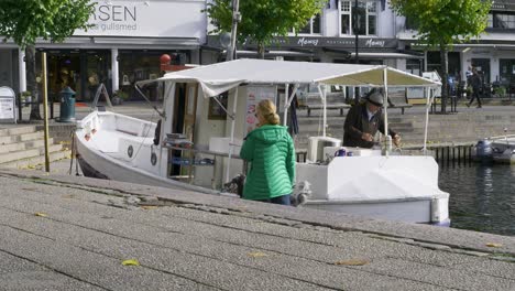 Fisherman-preparing-crabs-for-sale-off-his-boat,-a-woman-in-a-green-jacket-with-a-dog-passes-by