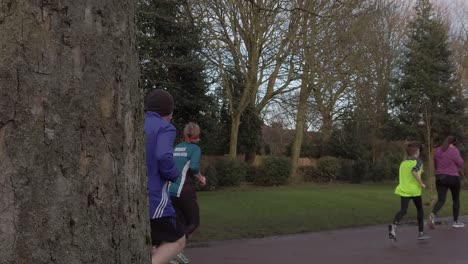 Active-fitness-group-jogging---walking-in-wet-rainy-park-in-slow-motion-behind-tree-view