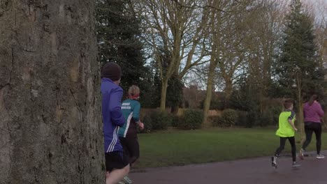 Jogging-Activo-En-Grupo---Caminar-En-Un-Parque-Húmedo-Y-Lluvioso-En-Cámara-Lenta-Detrás-De-La-Vista-Del-árbol